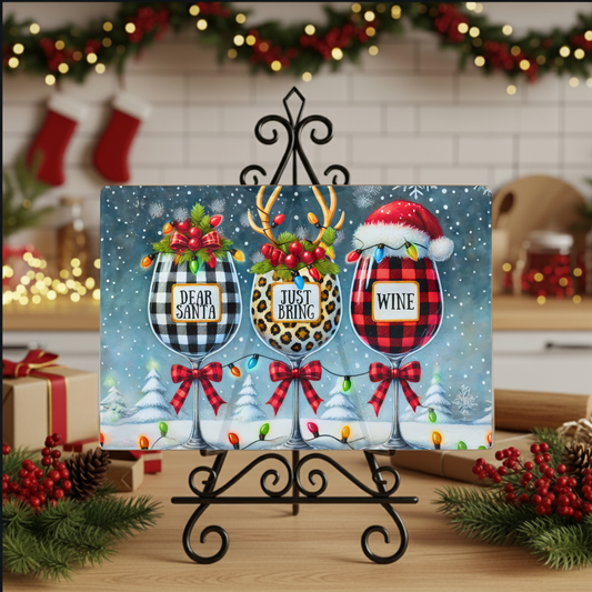 Personalized Christmas glass cutting board with three wine glasses in buffalo plaid, leopard and Santa hat designs, displayed on an easel in a holiday kitchen