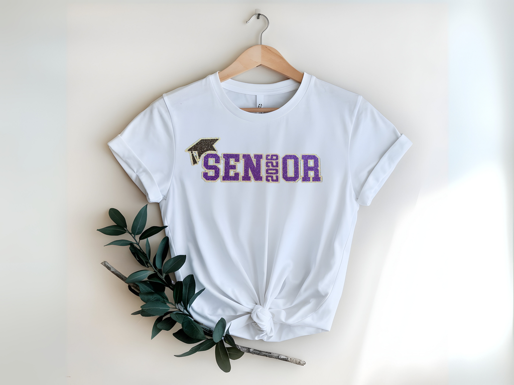 White t-shirt with 'Senior 2026' text and graduation cap graphic on a hanger.