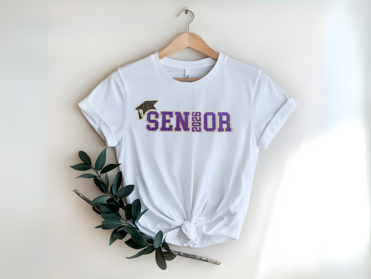 White t-shirt with 'Senior 2026' text and graduation cap graphic on a hanger.