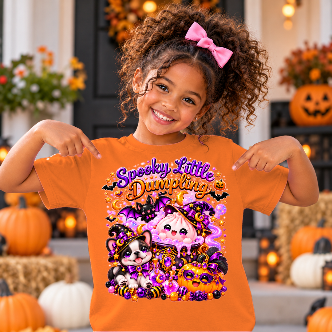 Girl wearing orange Spooky Little Dumpling Halloween tee on a fall porch with pumpkins